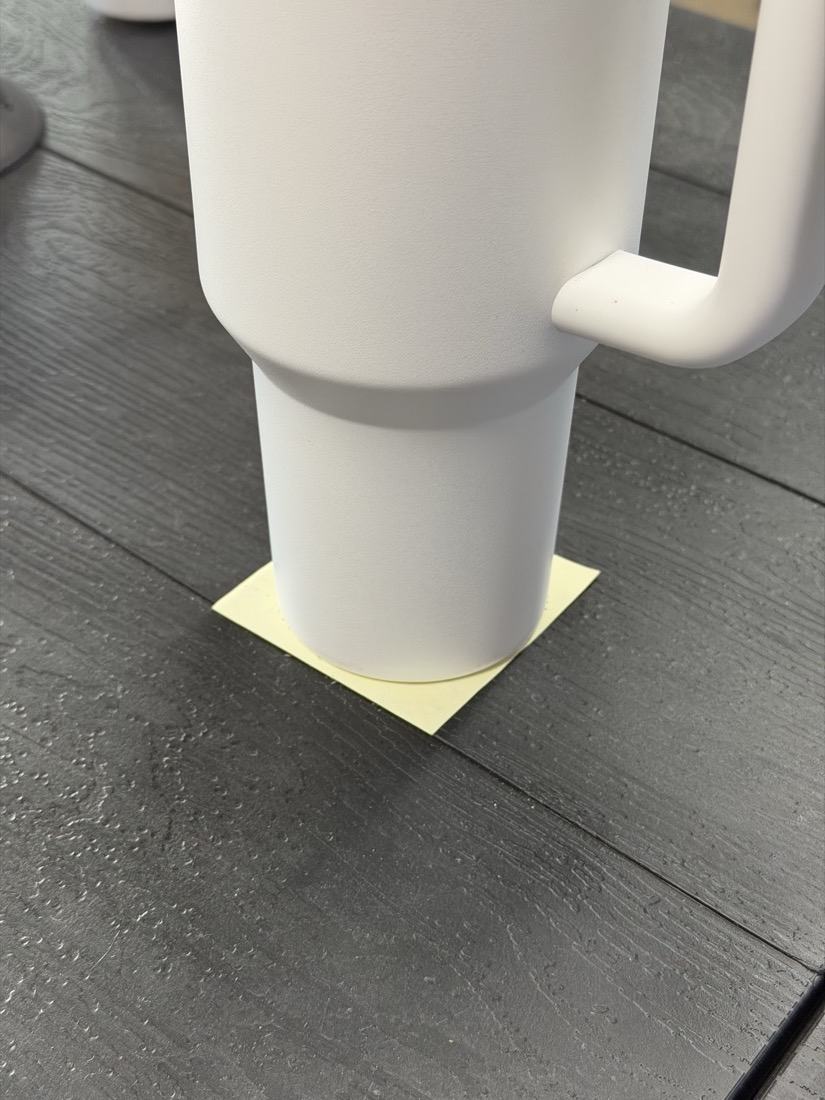 The base of a tumbler standing on a yellow sticky note, its base sitting within the width of the paper.