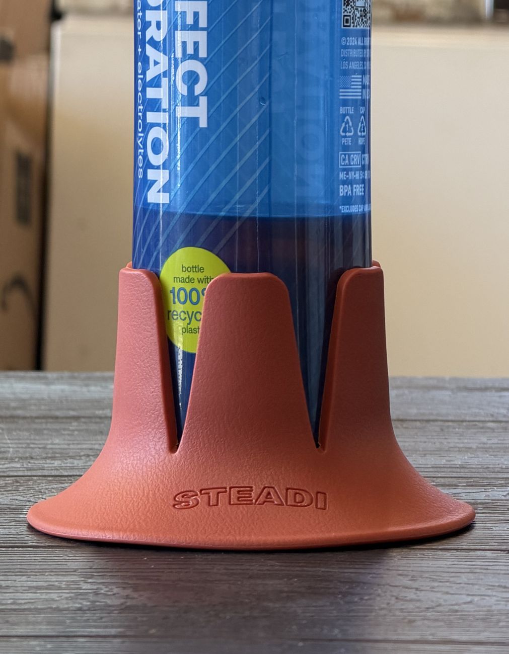 A narrow water bottle standing in a wide terracotta Steadi base on a table.